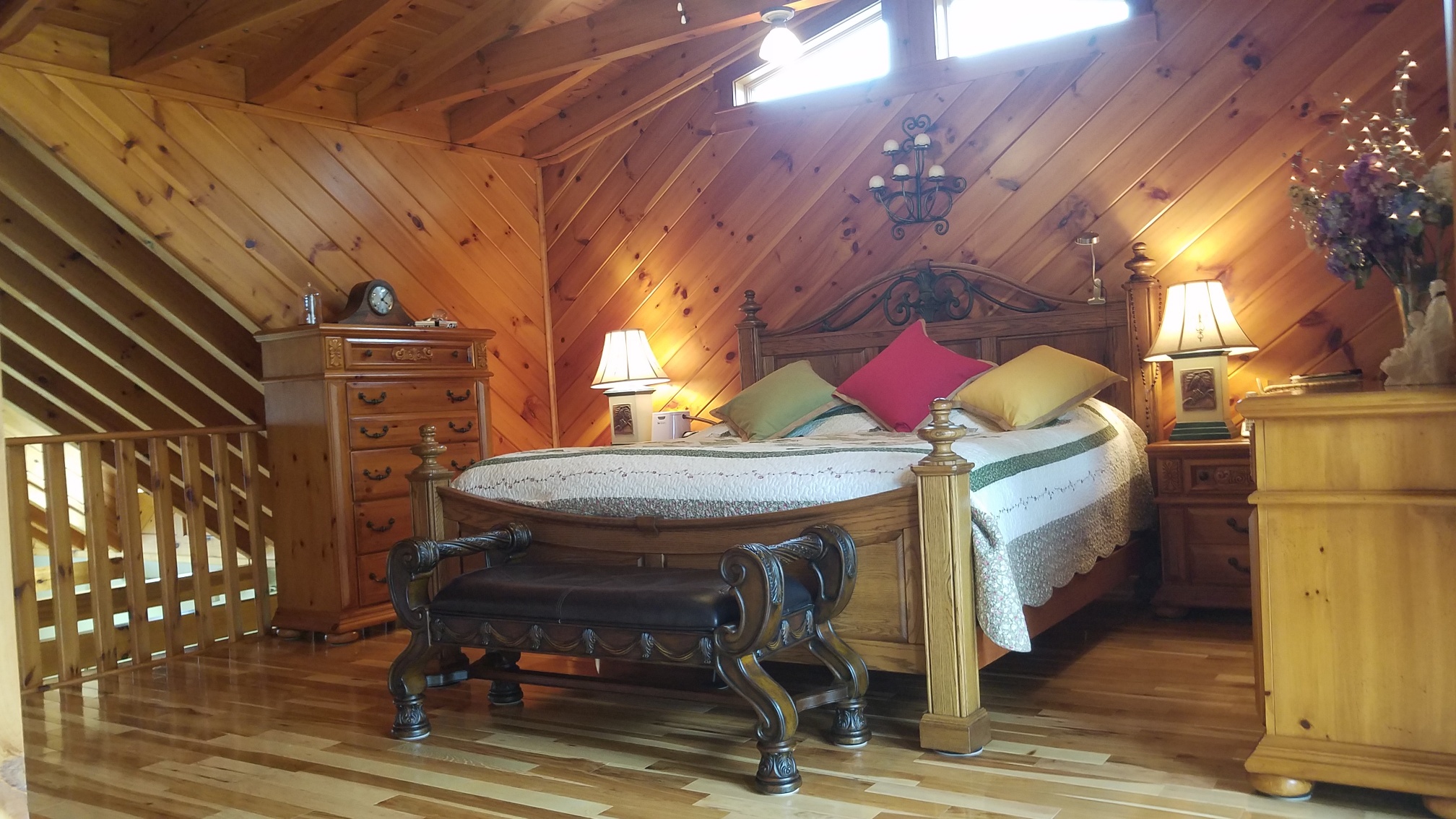 Loft bedroom with natural wood paneling, rustic furniture, and solid Appalachian hardwood flooring featuring warm grain variation from Turman Hardwood Flooring.
