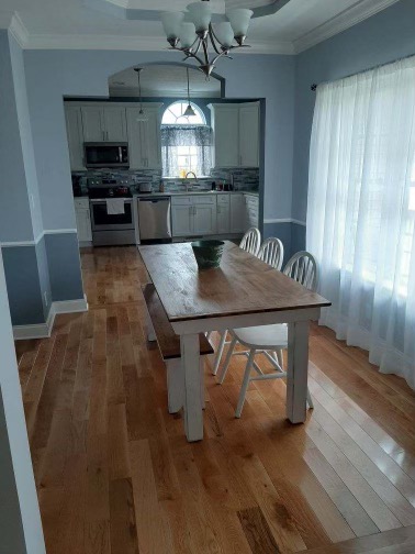 Dining room with Mill Run Natural Red Oak flooring and white chairs around the kitchen entrance toekick.