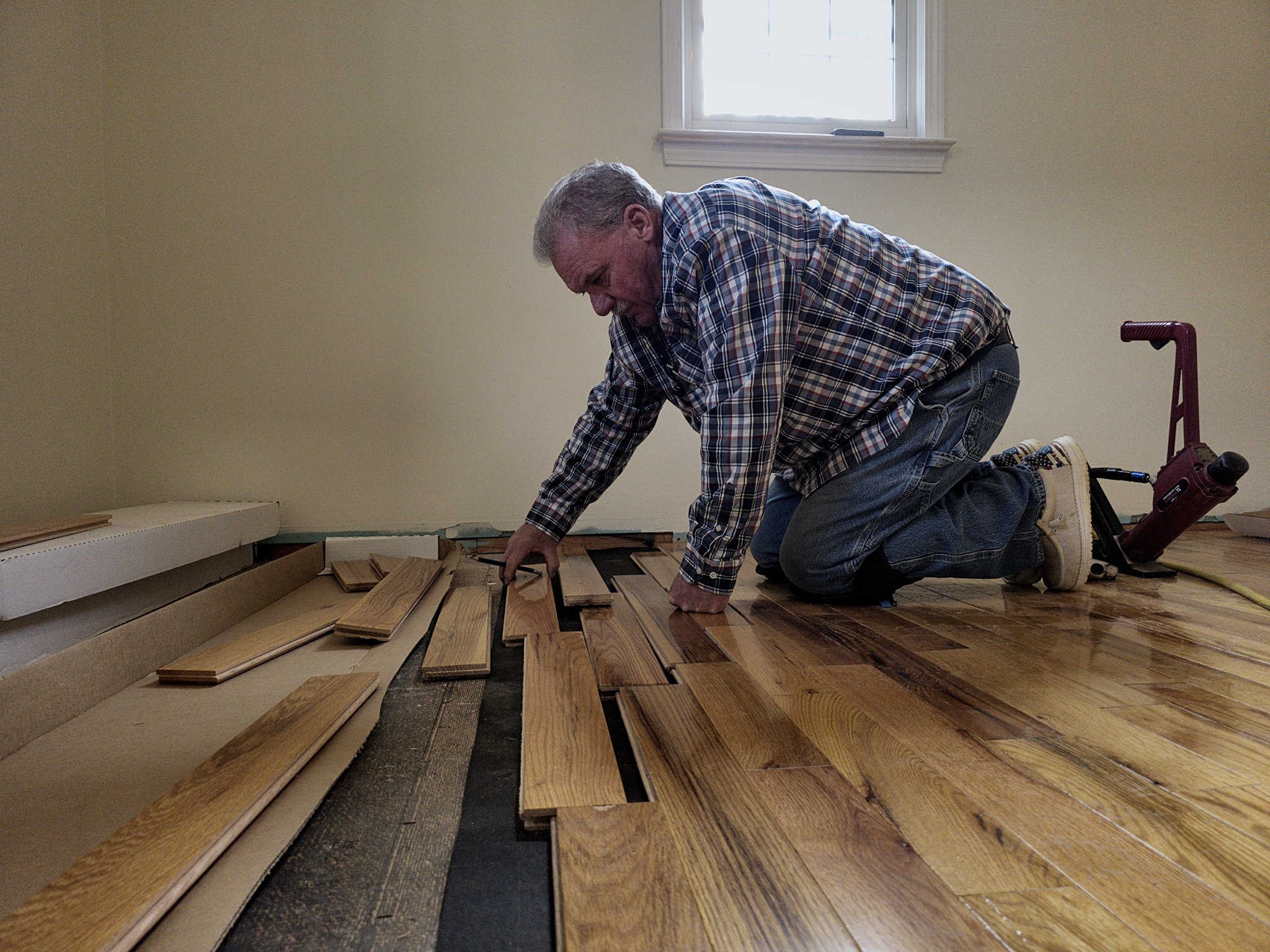 Professional contractor installing Turman Appalachian solid prefinished golden oak hardwood flooring planks using a pneumatic flooring nailer in a residential home.